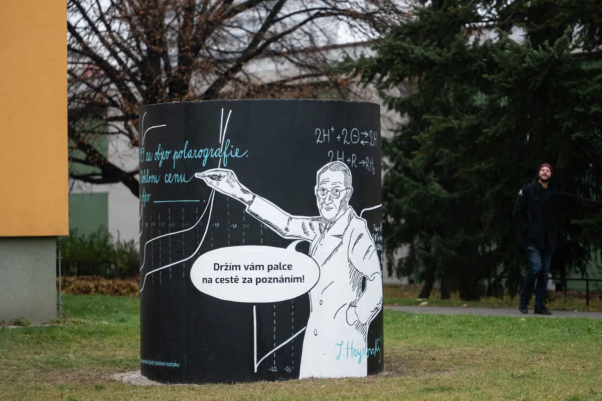 Mural on a concrete cylinder: a drawing of Jaroslav Heyrovský in a white coat pointing at a polarographic curve and chemical equations, with a speech bubble reading “I’m keeping my fingers crossed for you on your journey to knowledge!”