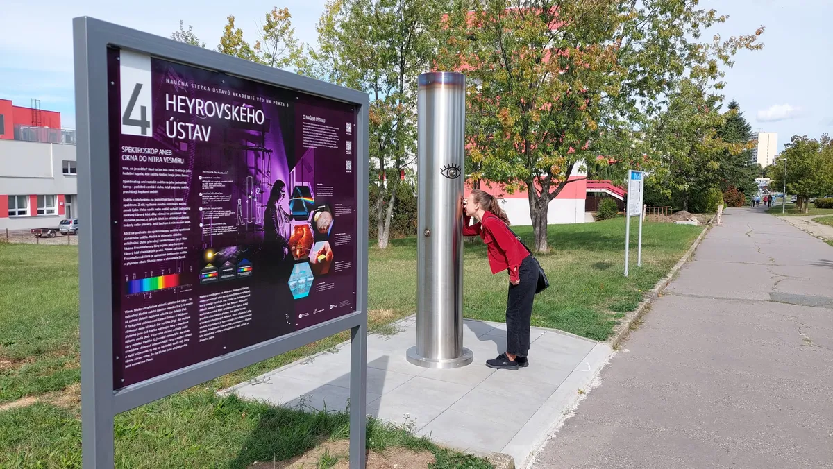 A visitor looks into the eyepiece of the stainless-steel spectroscope column, with the information panel of stop 4 at the J. Heyrovský Institute on the left