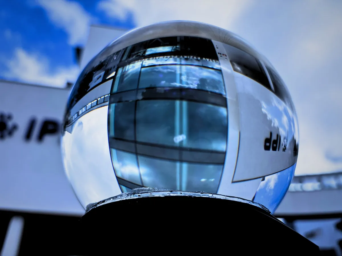 Close-up of the glass sphere of the atom model, reflecting the Institute of Plasma Physics building with the IPP logo and a blue sky